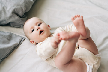 Adorable baby girl playing with her feet on white bed sheet.