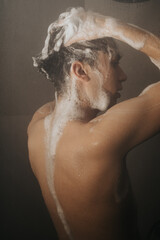 Close-up image of a young man lathering his hair with shampoo, capturing a moment of everyday personal care and hygiene in the shower.