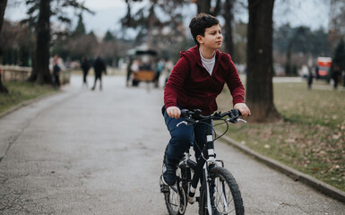 Carefree young boy riding a bicycle in a city park, surrounded by nature and enjoying a relaxing...
