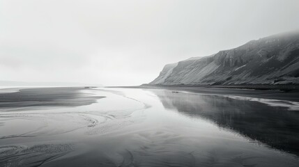 b'Black and white photo of a beach with a large cliff in the distance'