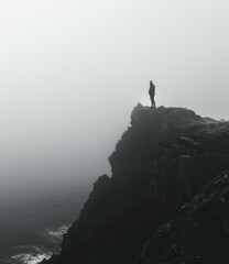 b'Man standing on a cliff overlooking a foggy sea'