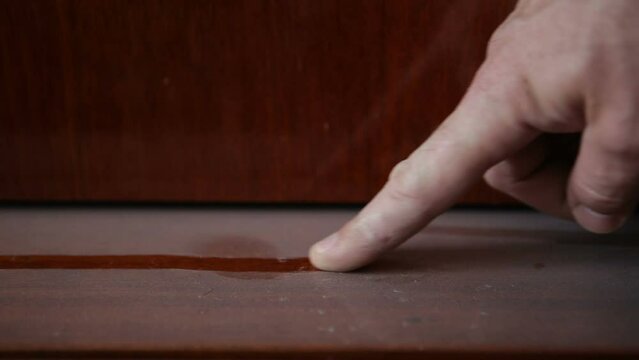 Dust in the apartment. A man runs his finger across the sideboard covered with dust.