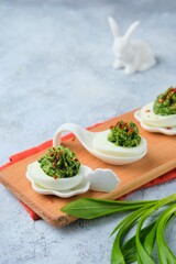 Cold appetizer, eggs stuffed with wild garlic, on a wooden board on a gray concrete background.