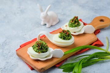 Cold appetizer, eggs stuffed with wild garlic, on a wooden board on a gray concrete background.