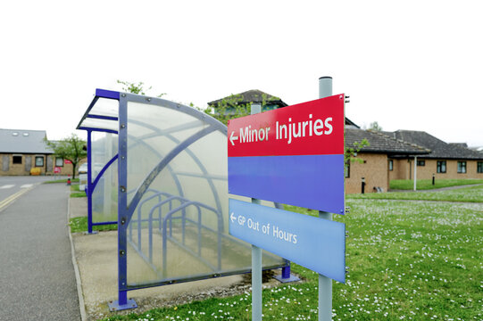 Shallow focus of a Minor Injury sign showing the way to the public treatment centre within the grounds of an NHS hospital in England. A public bike shelter can be seen next to the sign.