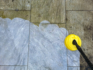 Pressure jet washer being used to clean porcelain tiles on a garden patio showing the difference...