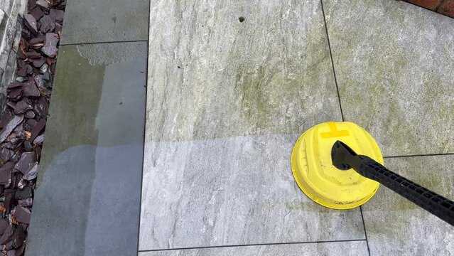 Pressure jet washer being used to clean porcelain tiles on a garden patio showing the difference before and after cleaning