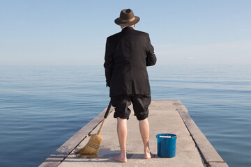 The back of an unidentified businessman in a black suit with pants rolled up sweeping a dock with a...