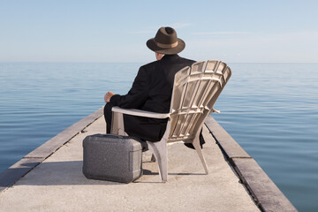 a unidentified  business man in a black suit sitting on a chair on a dock with a briefcase