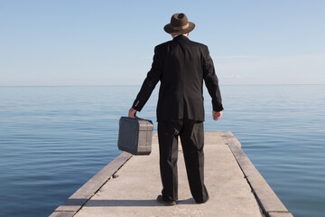 a unidentified  business man in a black suit standing on a pier looking out at the ocean holding a...