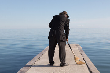an unidentified business man in a black suit sweeping a dock by the water