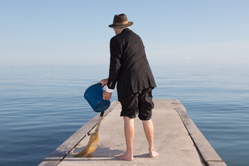 an unidentified businessman in a black suit and barefoot sweeping a dock with a bucket of water