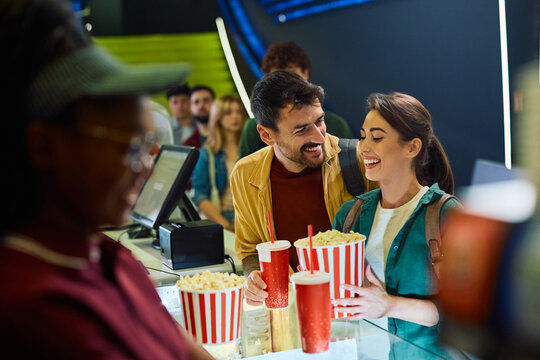 Young happy couple buying popcorn and drinks in cinema.