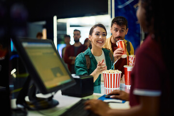 Happy woman buying popcorn before movie projection in cinema.