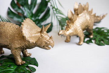 Golden dinosaur figurines and palm leaves on a white background.