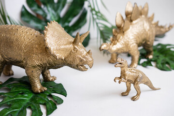 Golden dinosaur figurines and palm leaves on a white background.