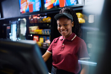 Happy black concession stand worker using computer in movie theater.