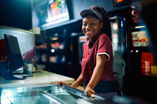 Happy black female cashier working in cinema and looking at camera.