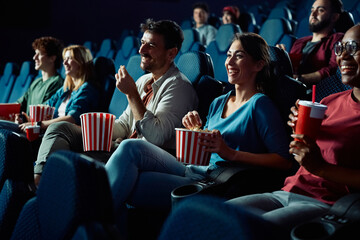 Cheerful woman eating popcorn while watching movie projection in cinema.