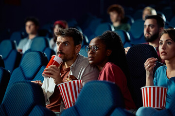 Young couple watching suspenseful movie in cinema.