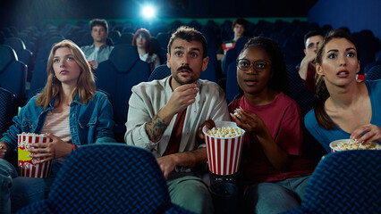 Group of people watching suspenseful movie in cinema.