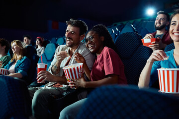 Cheerful couple laughing during film projection in movie theater.