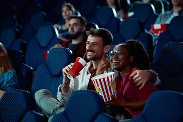 Happy multiracial couple watching movie on date night in cinema.