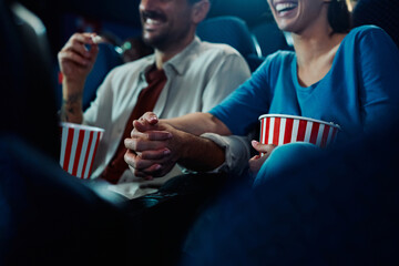 Close up of couple watching movie while holding hands in cinema.