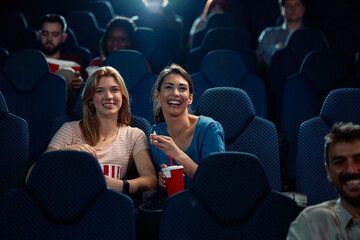 Happy female friends watching movie in cinema.