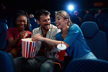 Cheerful friends eating popcorn watching movie in cinema.