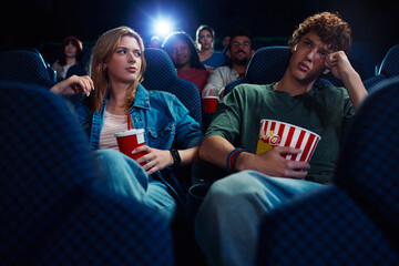 Bored man watching movie with is girlfriend in cinema.