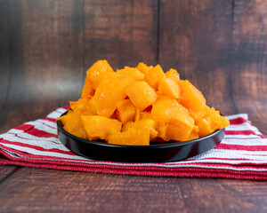Chopped papaya on a black plate. Wood background. Close-up detail.