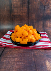 Chopped papaya on a black plate. Wood background. Chopped photo, in vertical format for social networks.