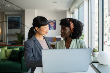 Two young businesswomen discussing work over laptop in office