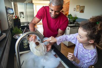 Father and daughter washing dishes together at home