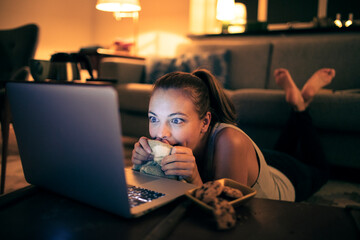 Woman watching movie on laptop with snacks at night