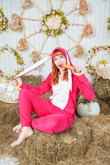 Beautiful redhaired woman wearing bunny costume eating carrot sitting on the haystack Easter holiday concept