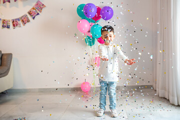 Joy fills the air as a young child plays with a burst of colorful confetti and balloons at a birthday party. Young boy beams with joy amidst a shower of colorful confetti, at his birthday celebration.