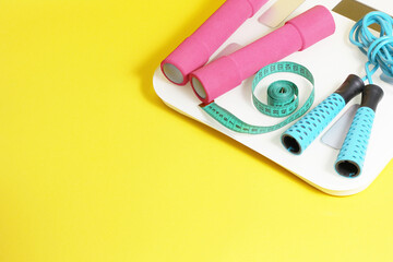Fitness items scales, jump rope, meter, dumbbells on a yellow background