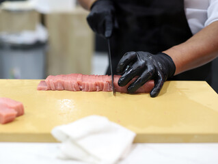 manos de chef con guantes negros cortando atún para hacer sushi - obrazy, fototapety, plakaty