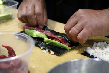 chef hands making sushi roll with avocado and red tuna