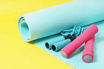 Fitness items jump rope, dumbbells and exercise mat on a yellow background