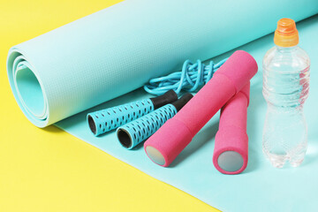 Fitness items jump rope, dumbbells, bottle of water and exercise mat on a yellow background