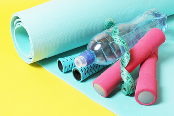 Fitness items jump rope, dumbbells, meter, bottle of water and exercise mat on a yellow background
