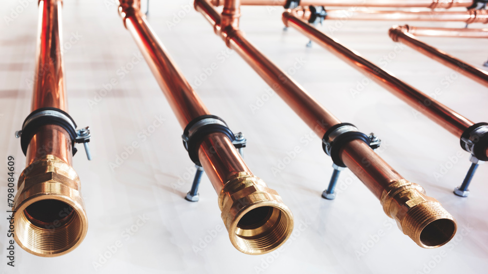 Poster A row of copper pipes are lined up on a white surface. The pipes are of varying lengths and are connected to each other. Concept of order and organization, as the pipes are neatly arranged in a row