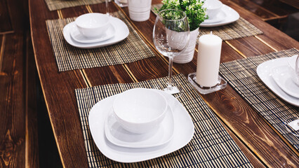A wooden table with a white tablecloth and a candle on it. The table is set with plates, bowls, and wine glasses