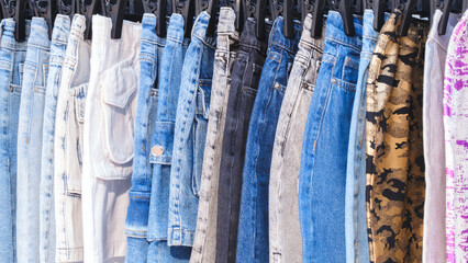 A row of jeans with different colors and patterns. The jeans are hanging on a rack
