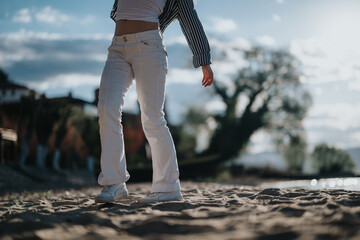 A person in white pants stands on a sandy beach, evoking a sense of calm and enjoyment on a sunny...