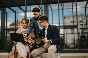 Three business professionals engaged in a collaborative discussion, outdoors with electronic devices, brainstorming success strategies.