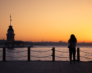 Silhouette of a young woman taking photos of the Maidens tower in a beautiful sunset in Istanbul....